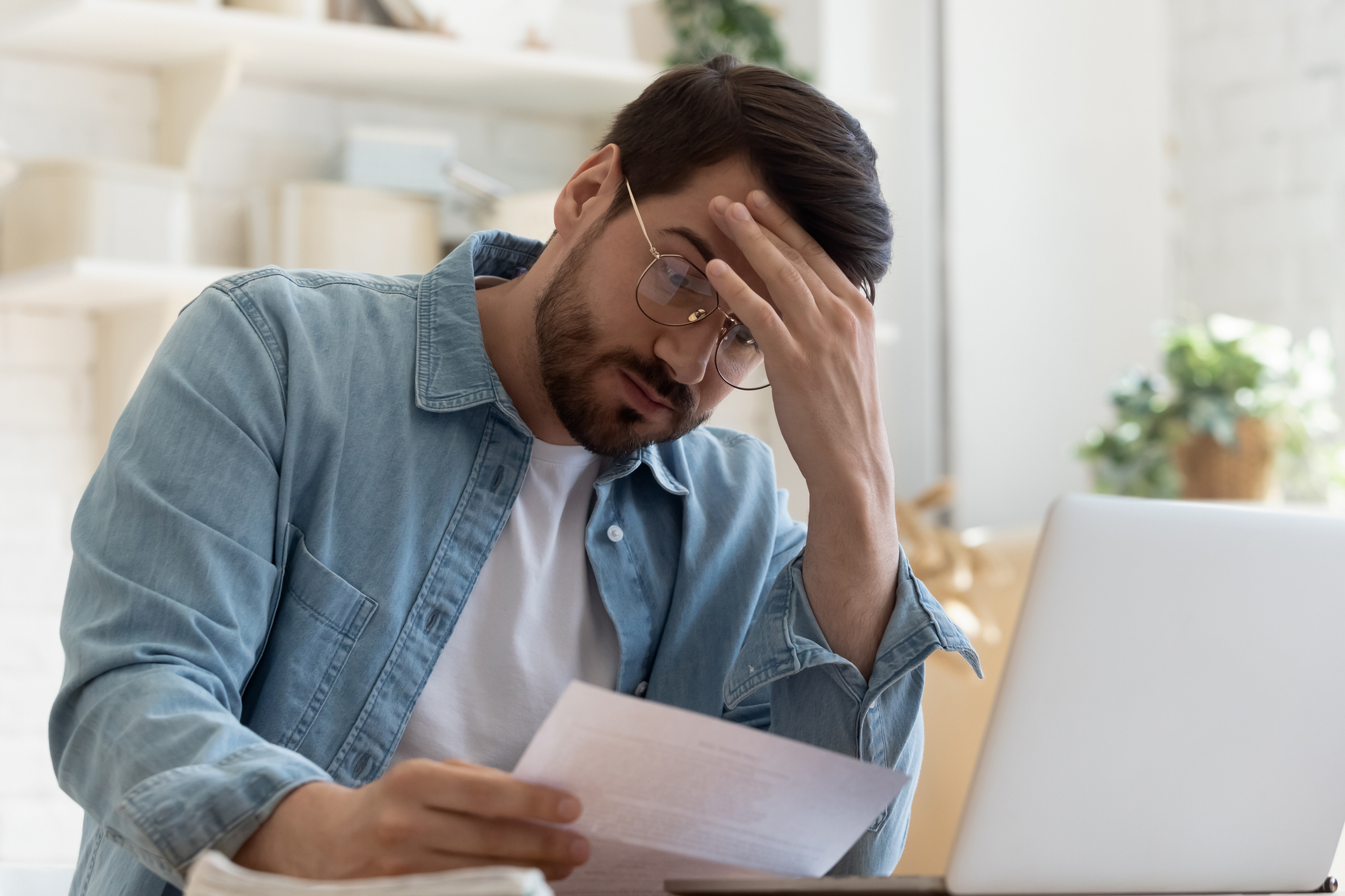 Man at laptop holding head while reading document
