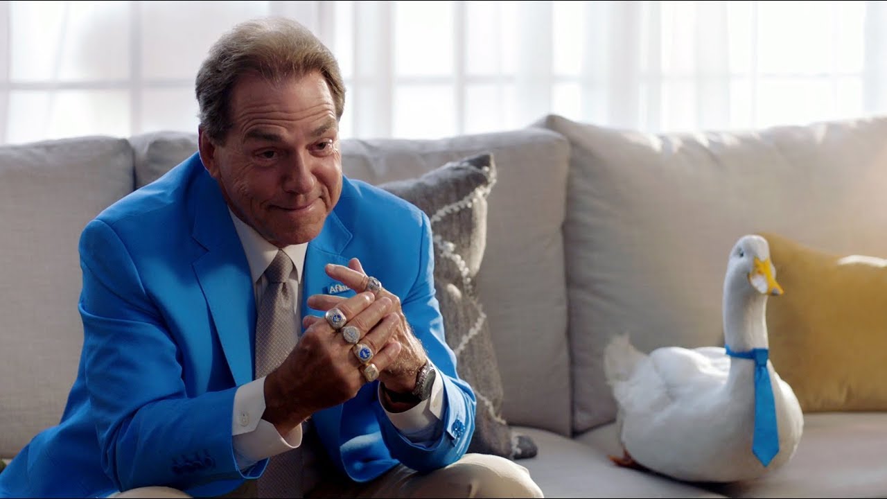 Coach Nick Saban on a couch with the Aflac duck mascot.