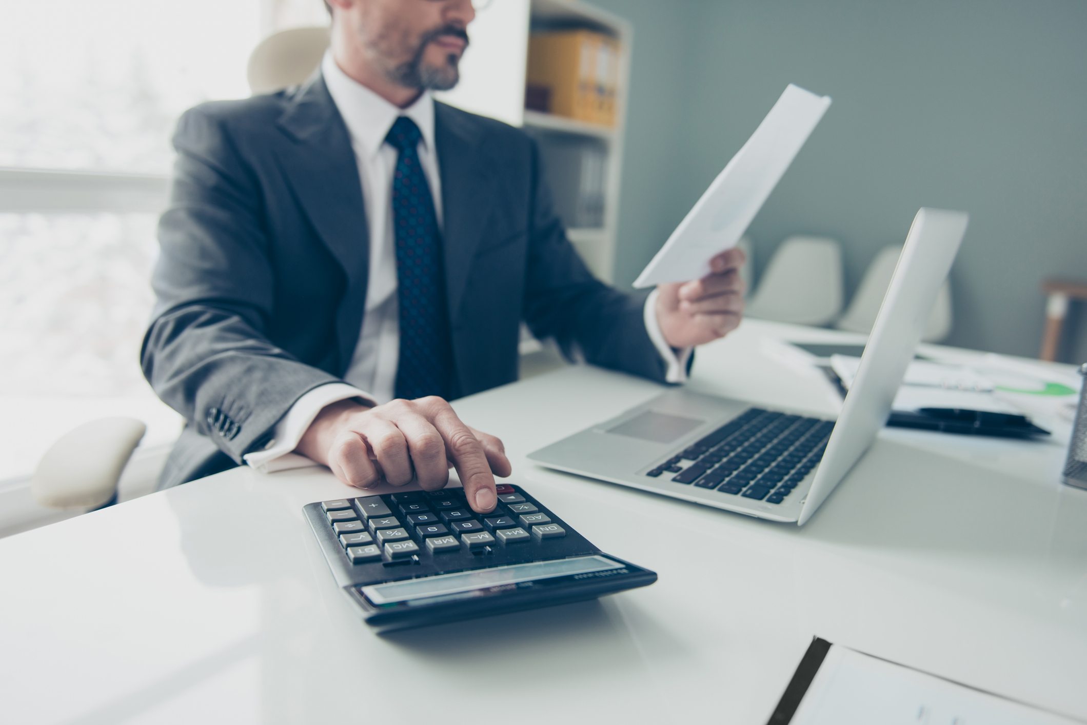 Man in suit reading a financial report and typing numbers into a calculator
