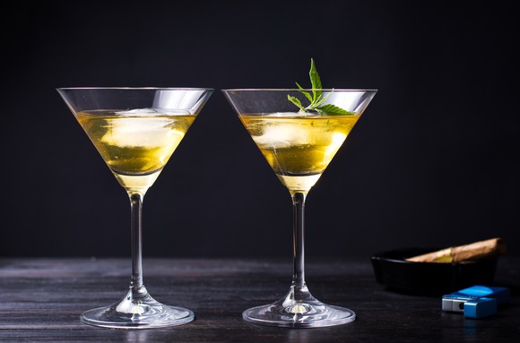 2 martini glasses filled with marijuana-infused drinks next to an ashtray and a lighter.