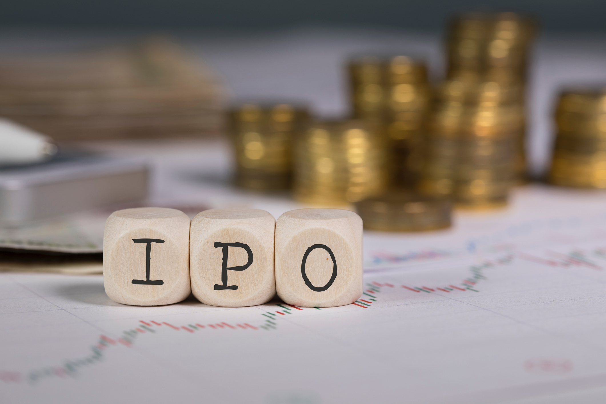 Blocks spelling IPO in front of stacks of coins on top of stock charts