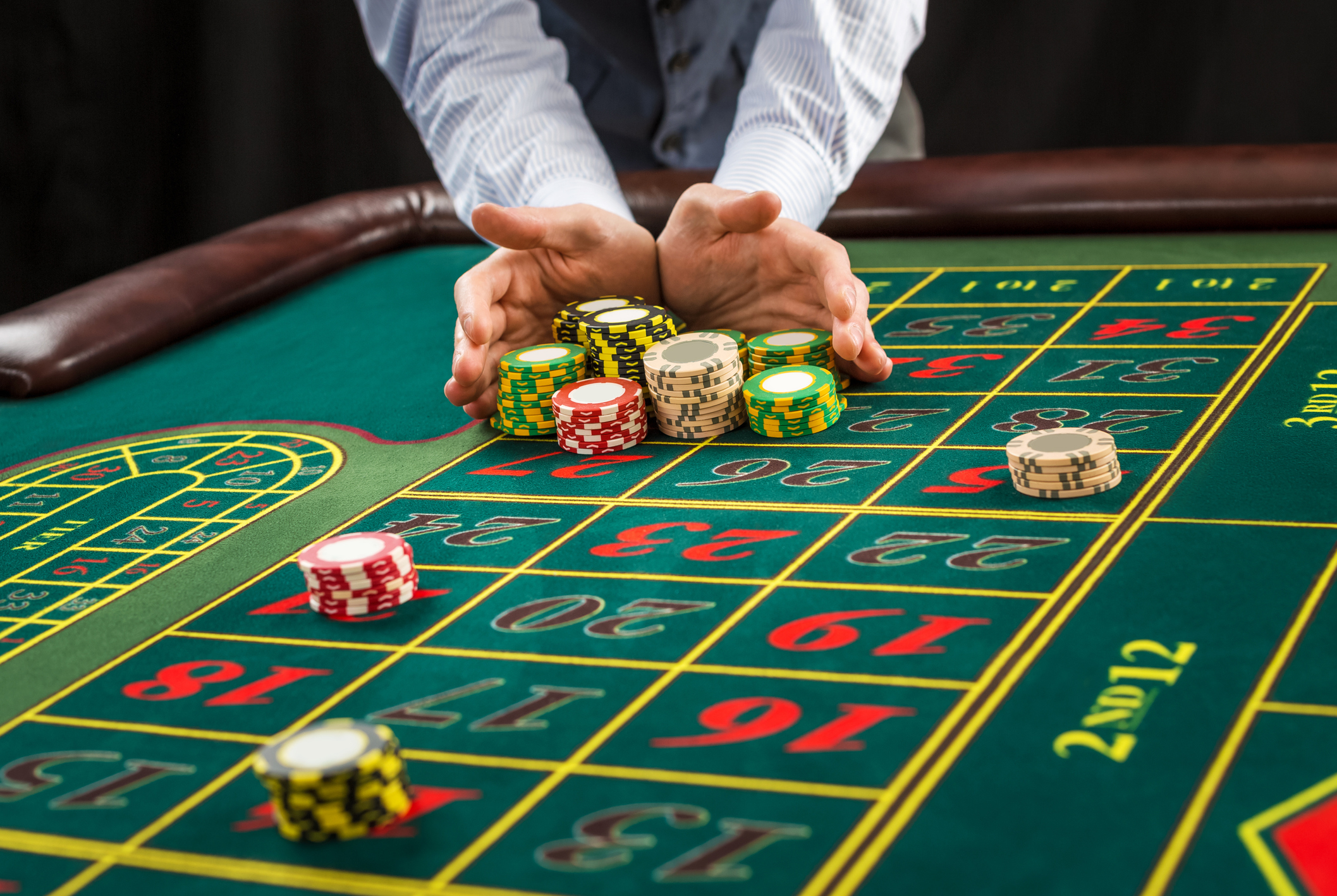 A casino dealer pushing chips to a player at the roulette table.