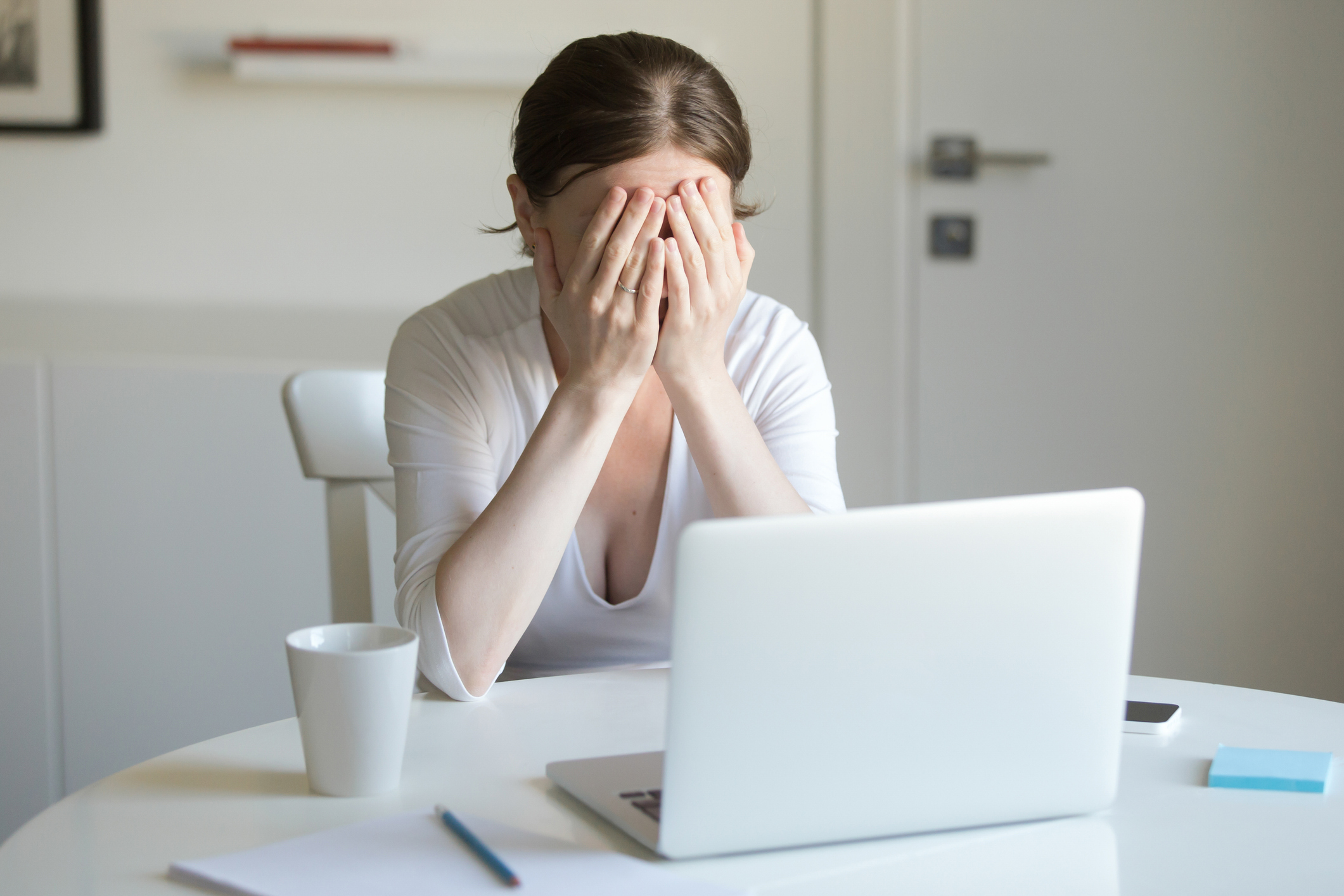 Woman sitting at laptop, covering her face