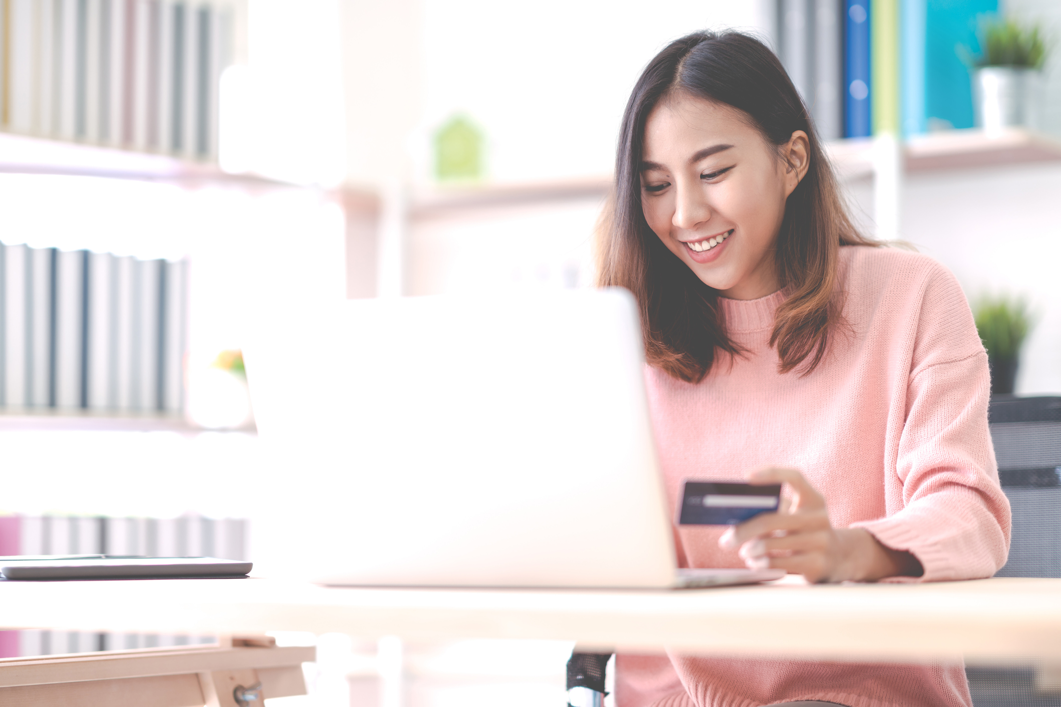 A young lady on her laptop holding a credit card in her left hand.