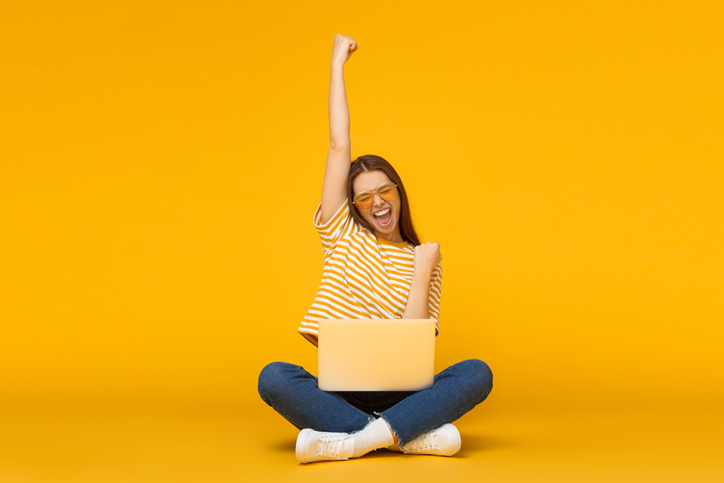 A woman pumping her fist in excitement as she sits with her laptop.