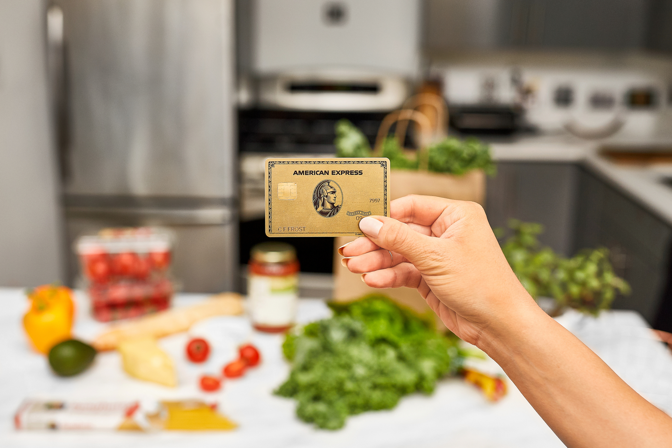 Hand holding an AmEx gold card while located in a kitchen.