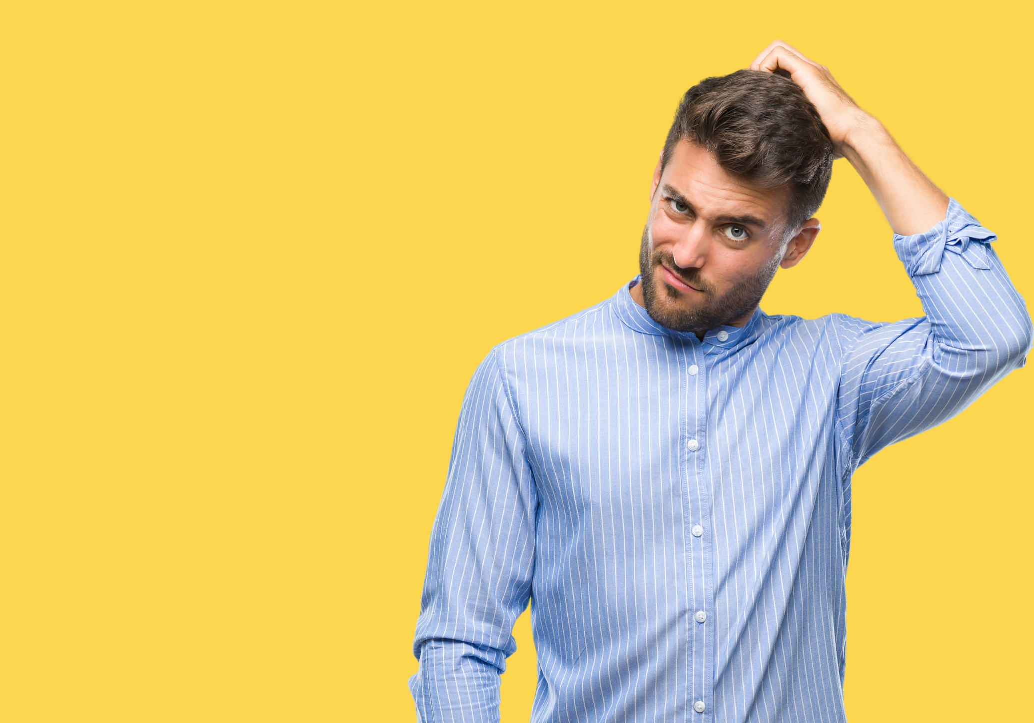 Man in collared shirt against yellow background scratching his head