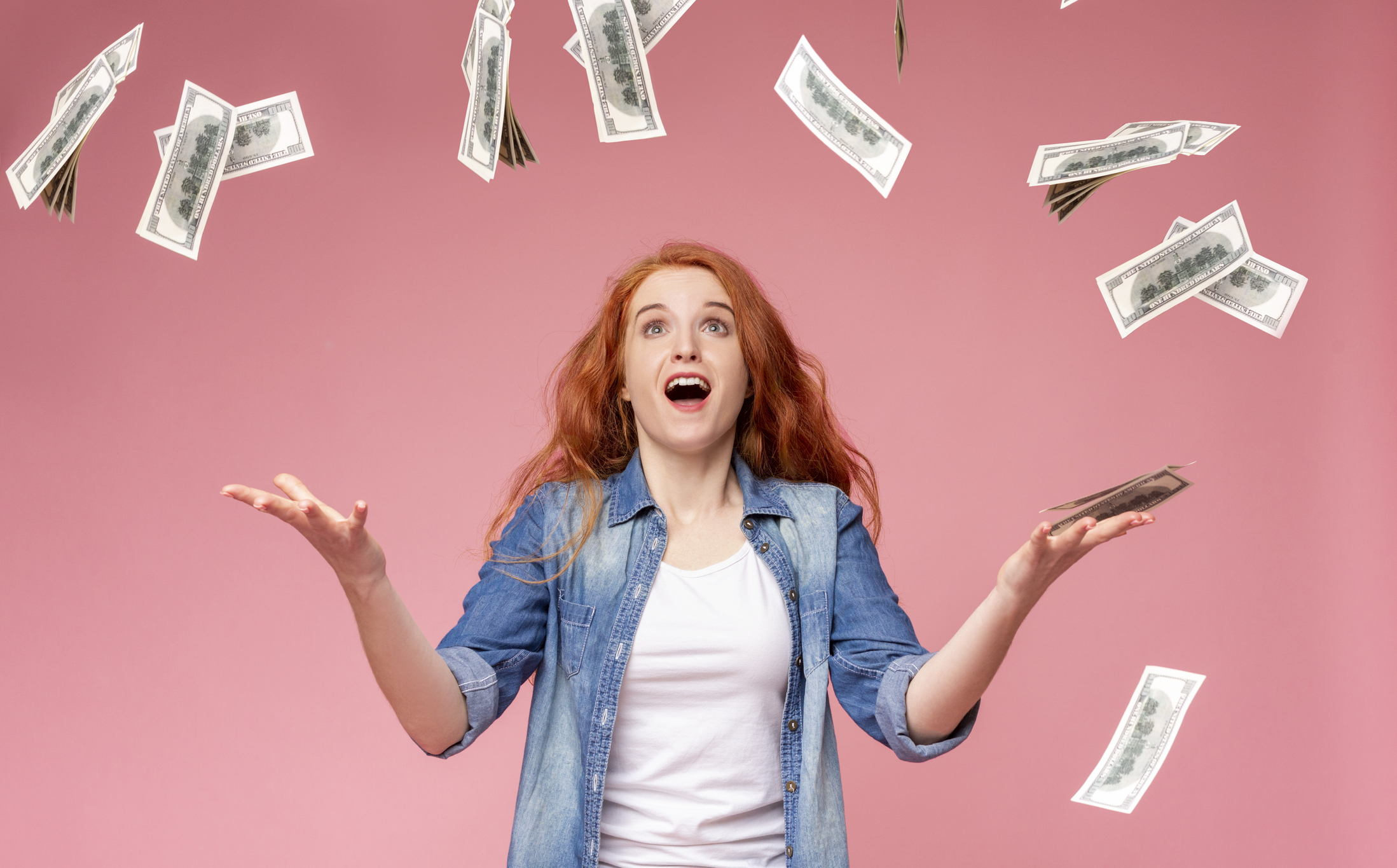 A young woman is surprised as hundred-dollar bills rain down from the sky.