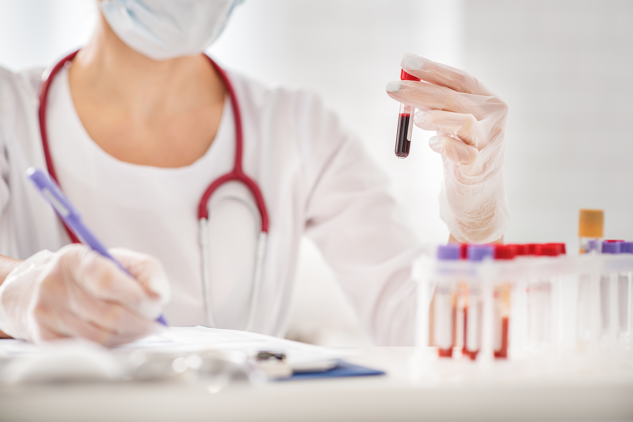A lab worker holds a test tube in one hand and writes notes with the other.