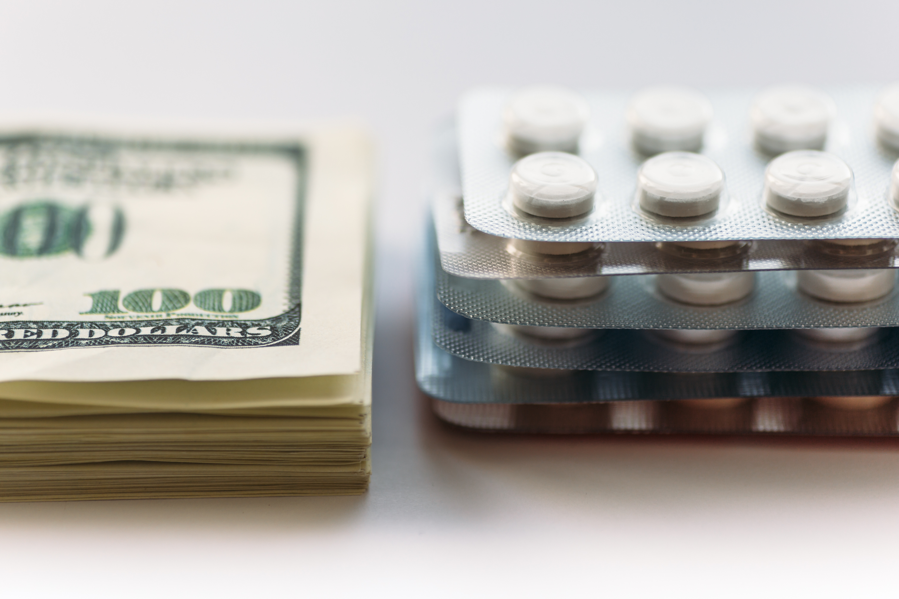 Stack of $100 bills next to stack of blister packs with white pills