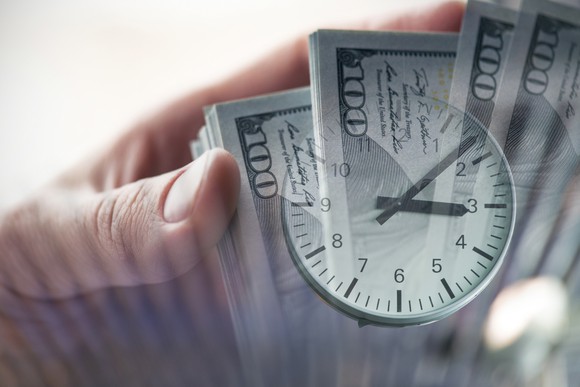 A person holding a stack of cash with a clock superimposed over the image