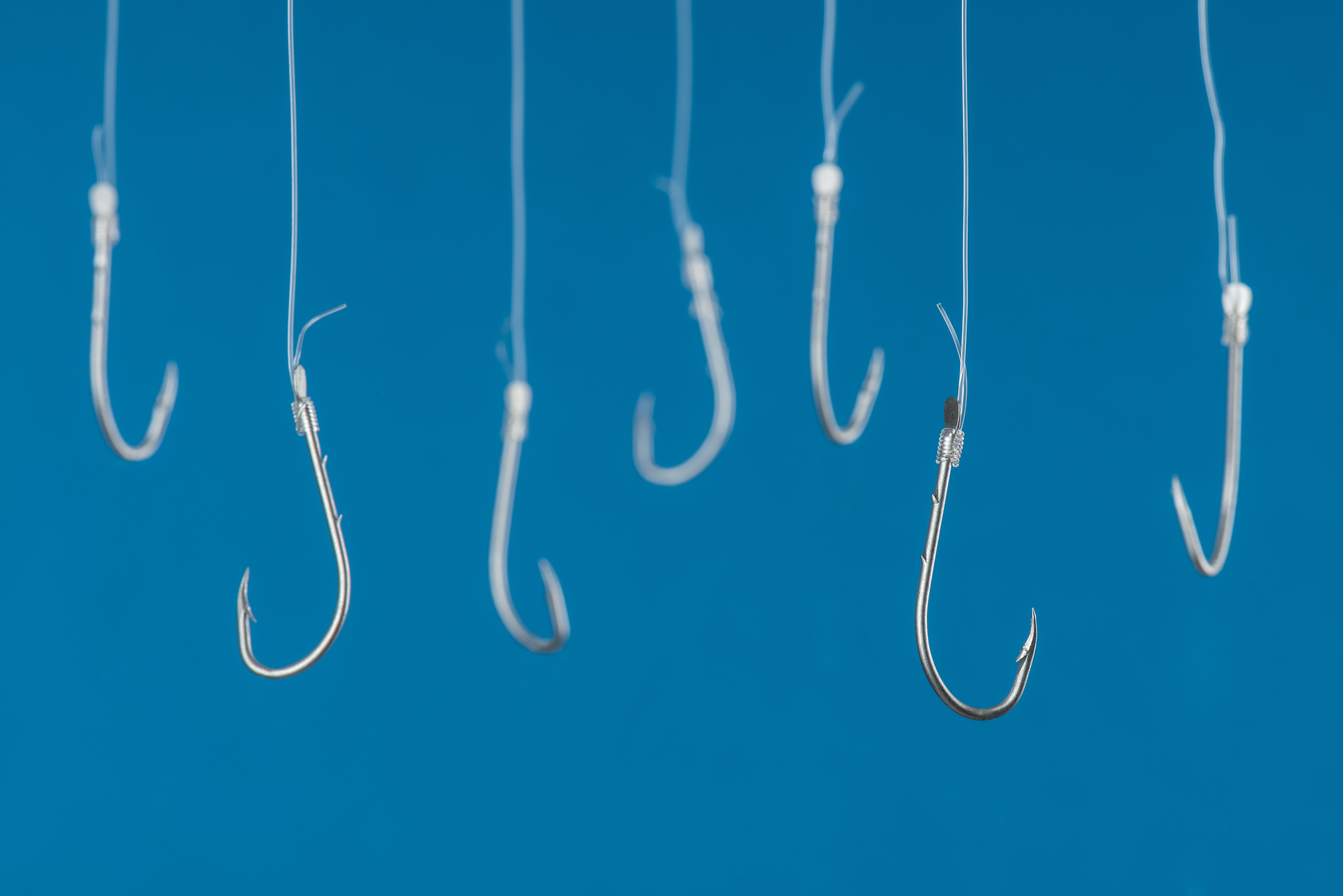 A series of fishing hooks tied to lines against a blue background.