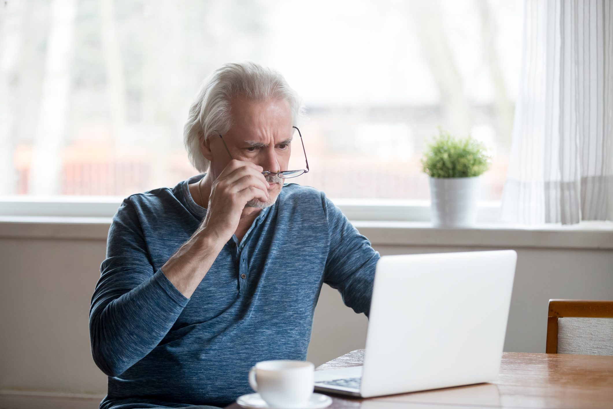 Shocked senior man removing glasses and looking at laptop