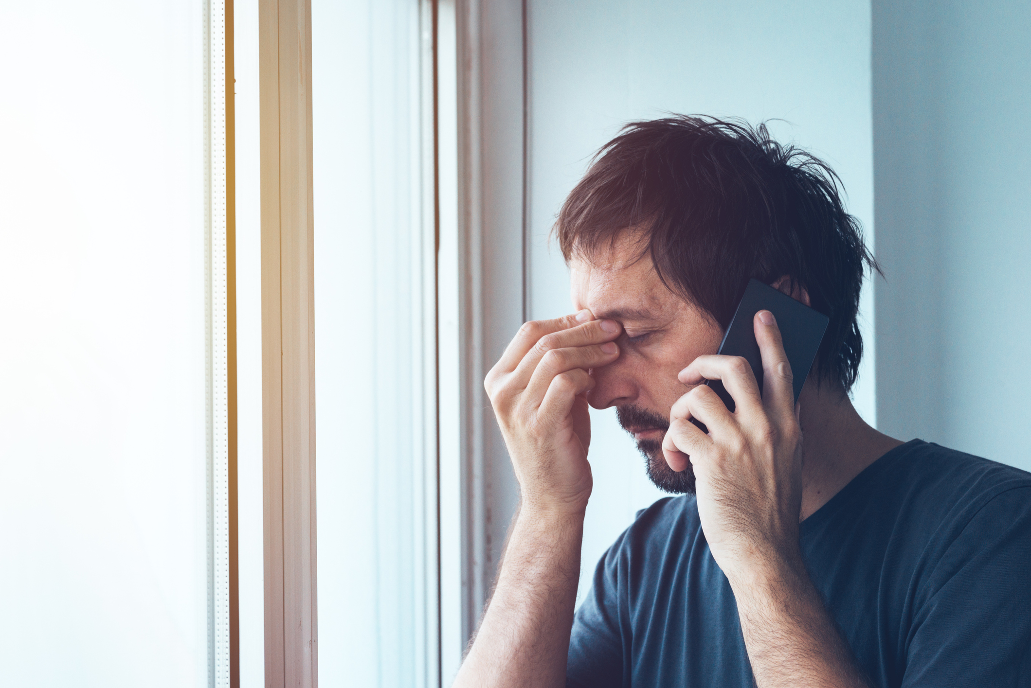 Man pinching his nose while holding cell phone to ear