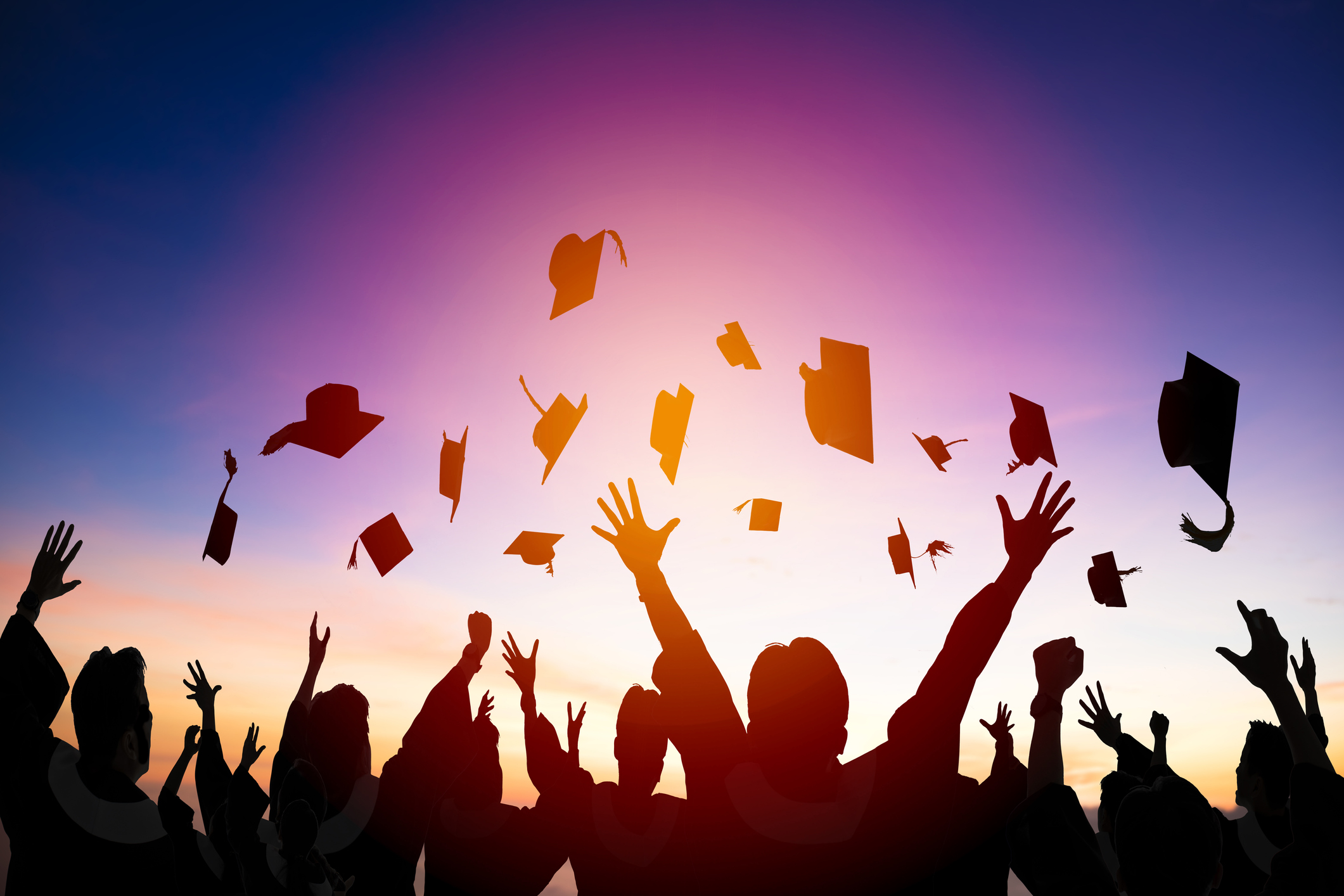 Silhouettes of graduates throwing up their graduation caps in front of a sunset.