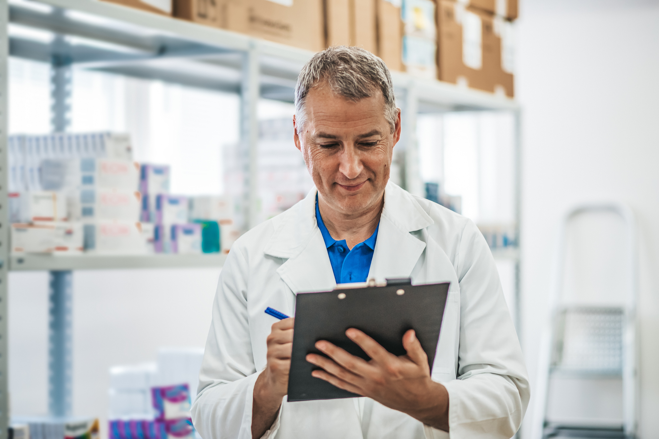Older man in white lab coat writing on clipboard