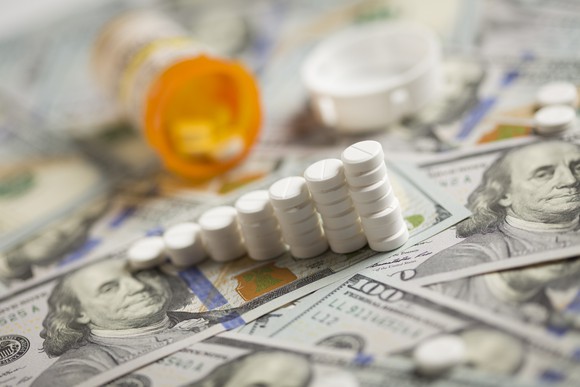 Ascending stacks of white tablets atop hundred dollar bills