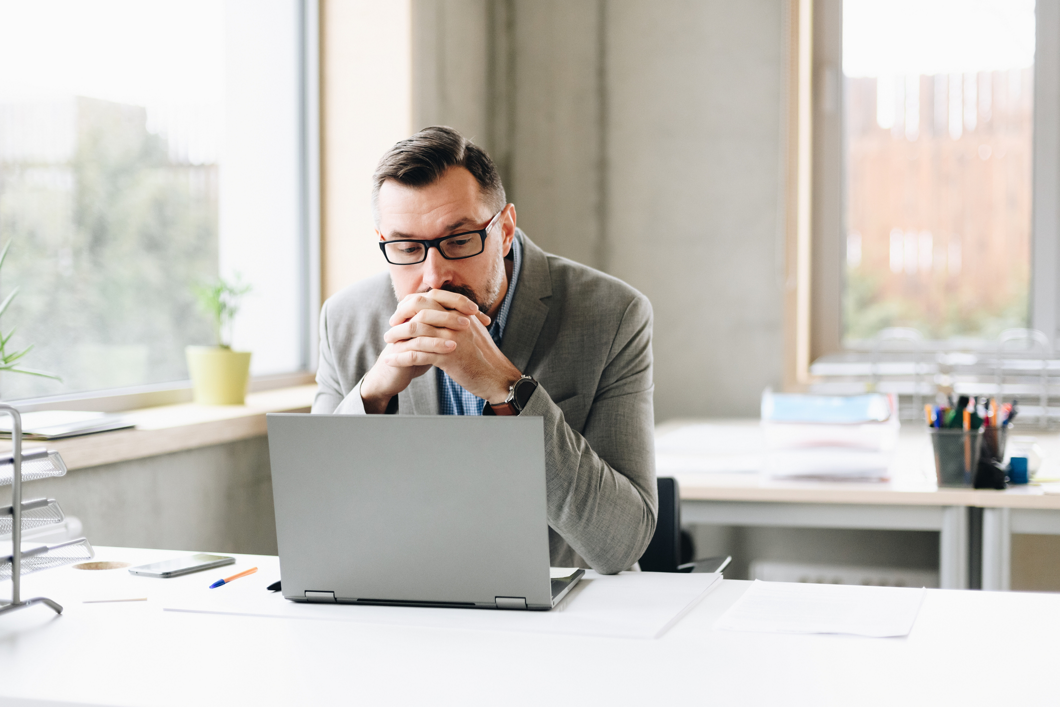 A man sits thoughtfully in front of a laptop at his desk.