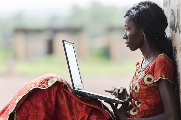 A young African woman uses a laptop outside.