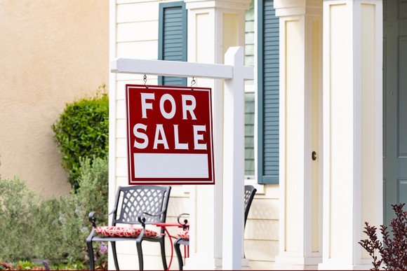 Front porch of home with for sale sign.