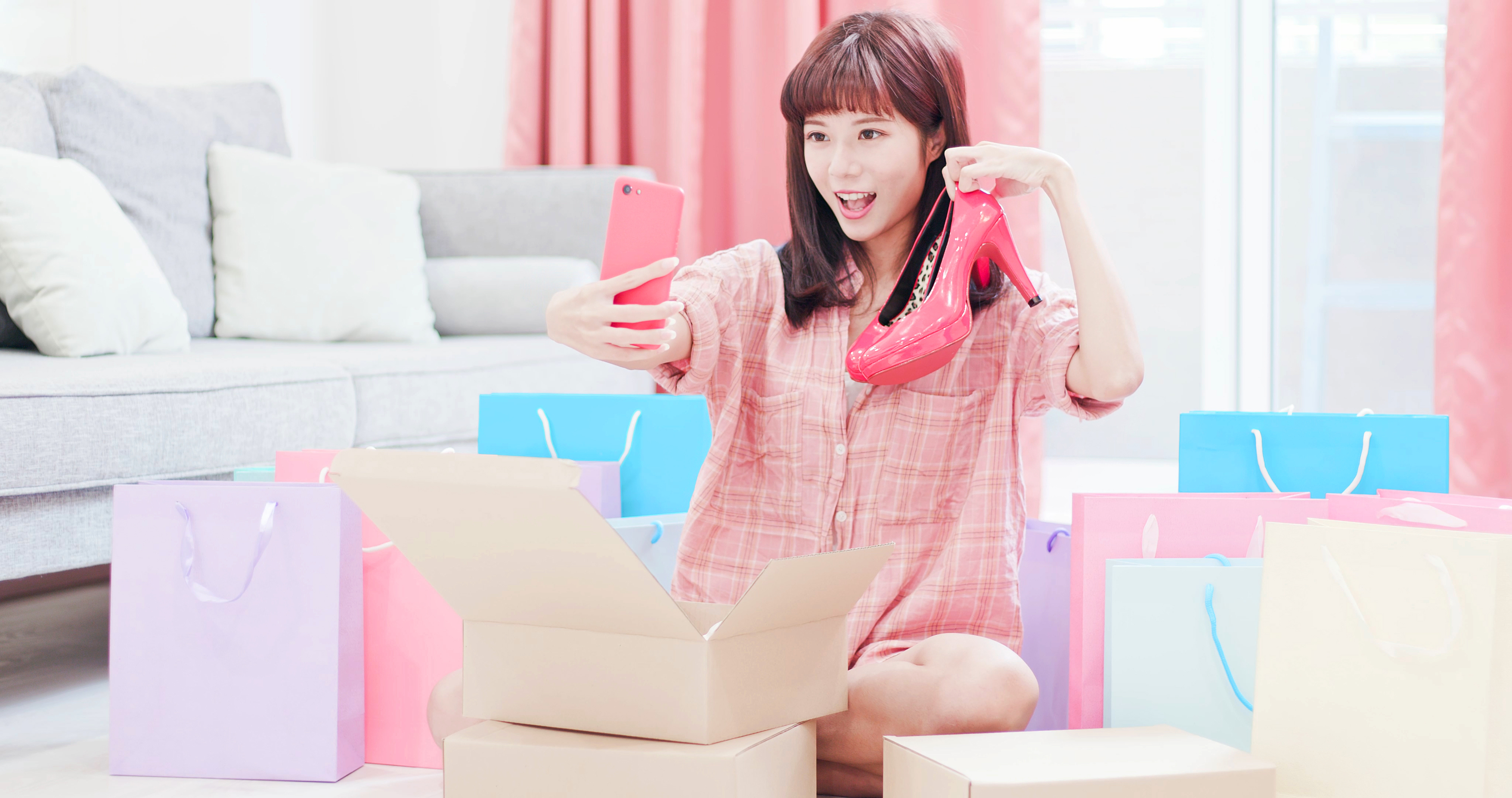 A young woman holds up a shoe and takes a selfie in her living room floor.