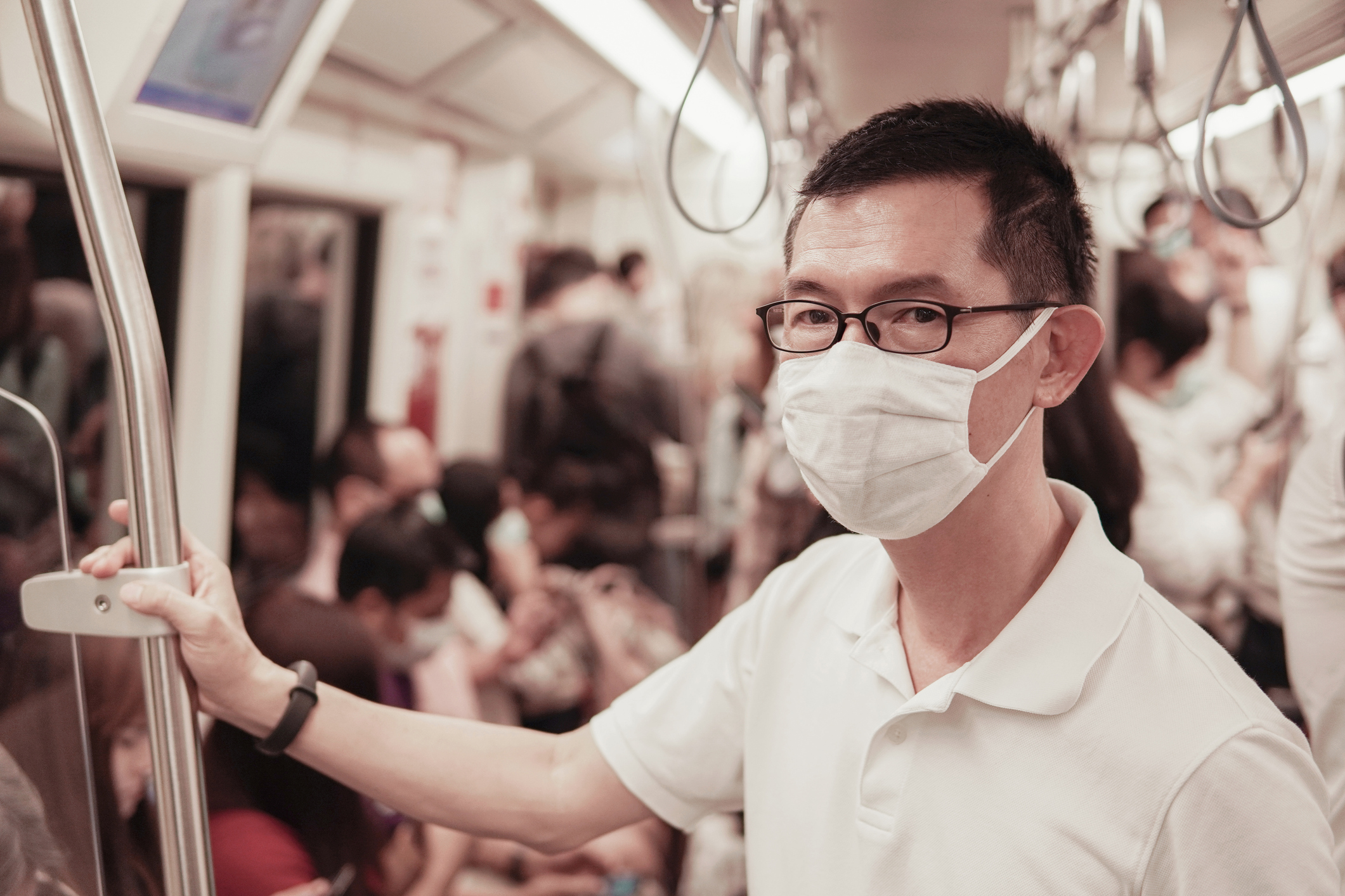 A man wearing a face mask while riding in a crowded subway car.