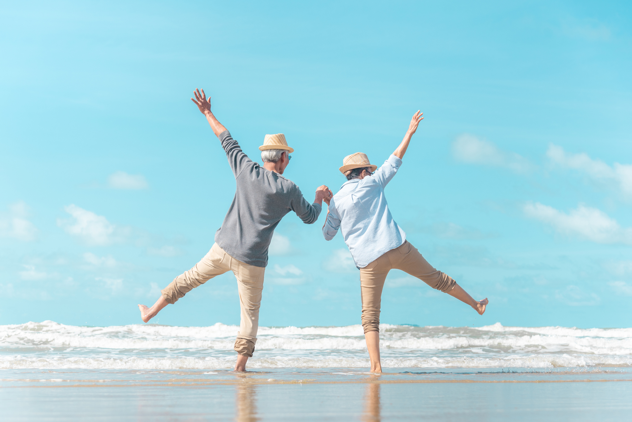 An older couple holding hands enjoying the beach.