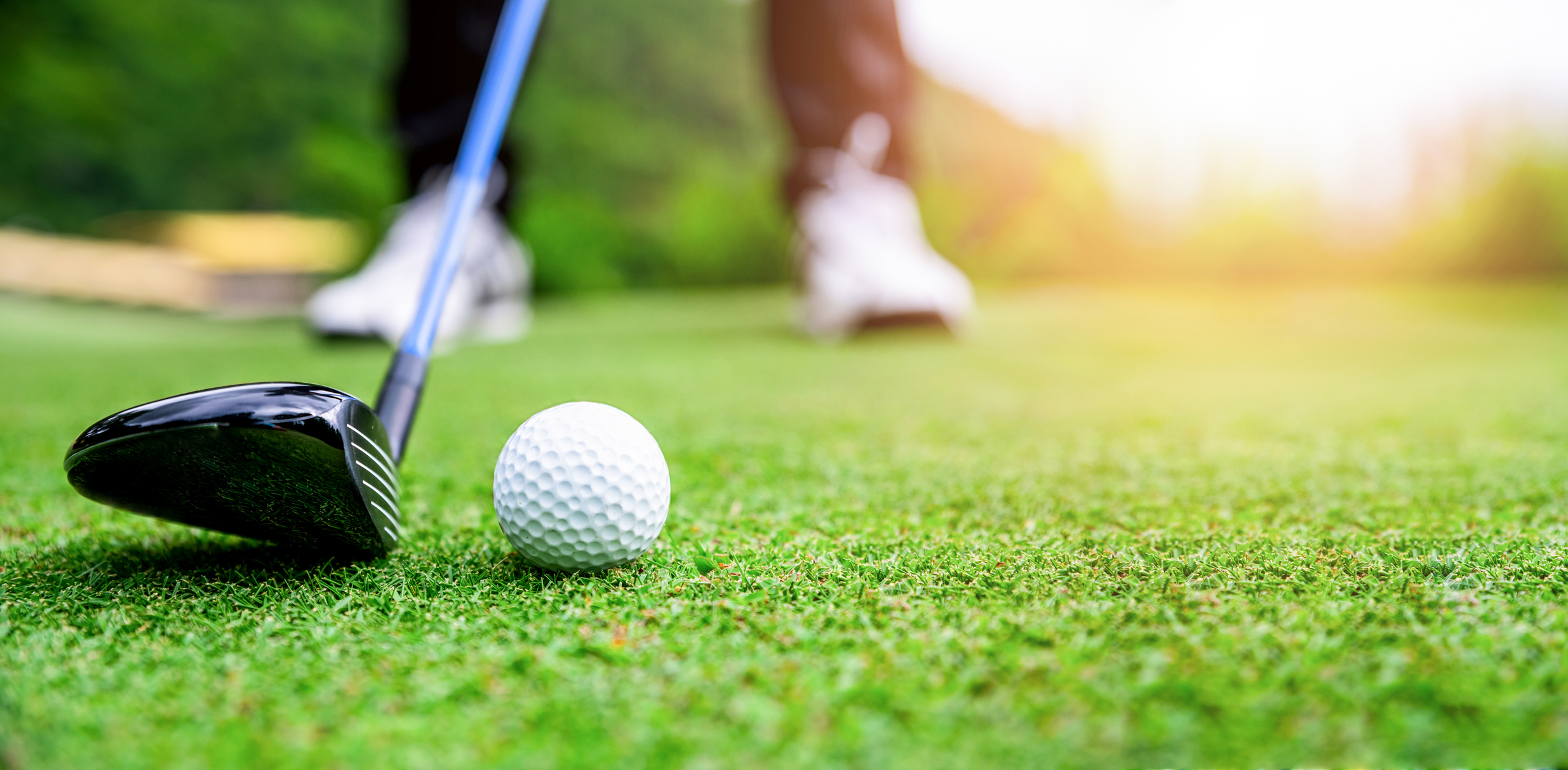 A close-up of a golf club about to hit a golf ball.