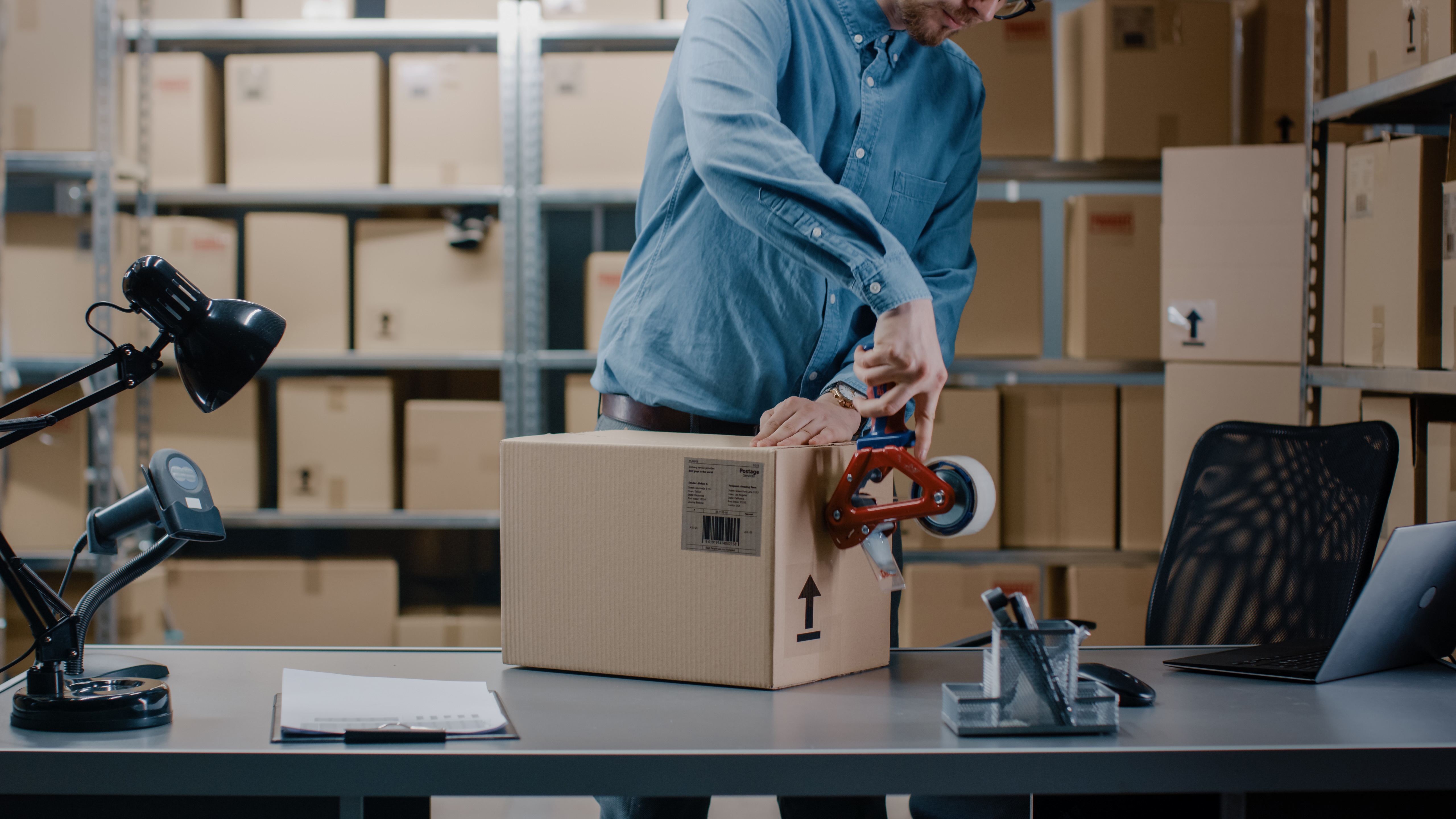 A man in a warehouse packing a box to ship.