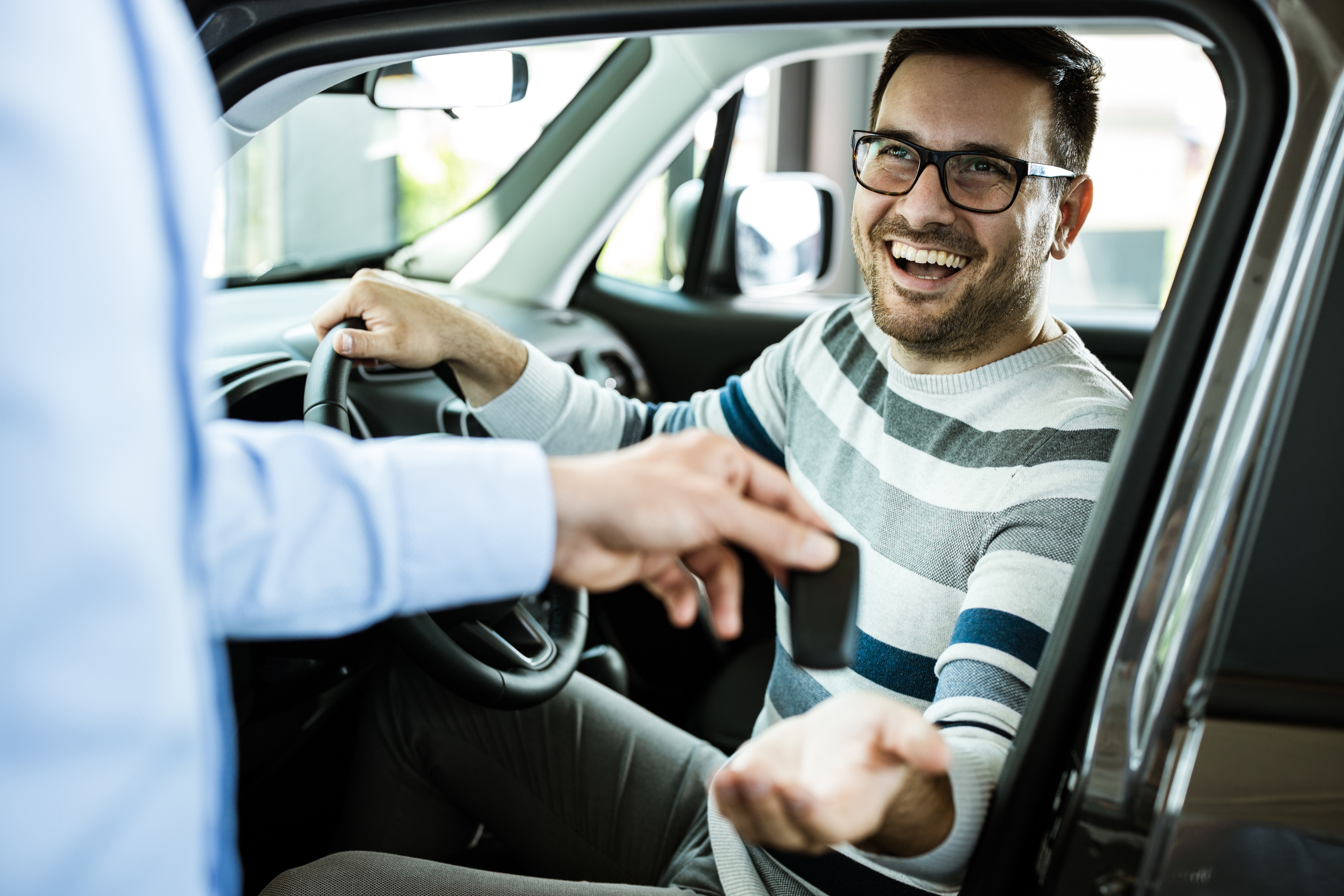 A man sitting in a car receives the keys from another person outside the car.