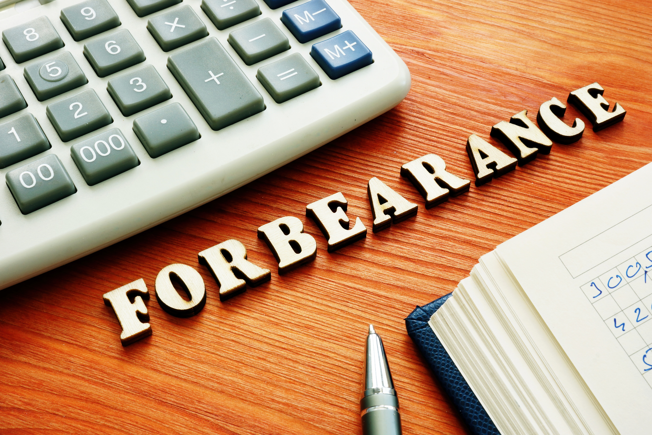 The word "forbearance" appears on a desk near a keyboard, book and pen.