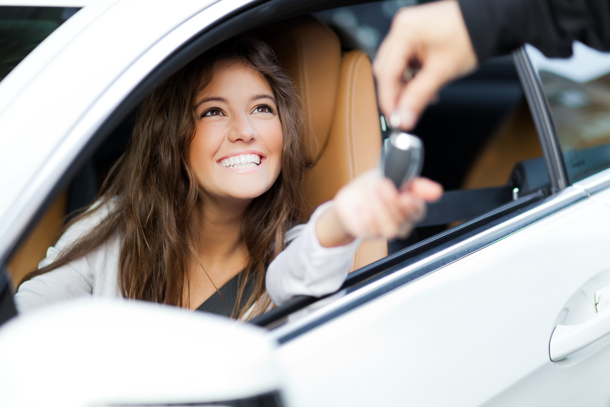 A young woman sitting in a car being handed the keys.