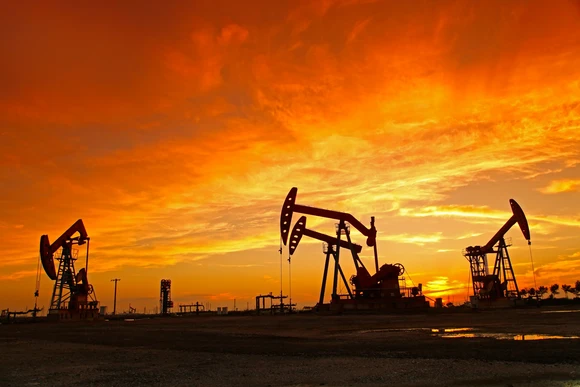 Several oil wells in a shadowed field near sunrise or sunset.