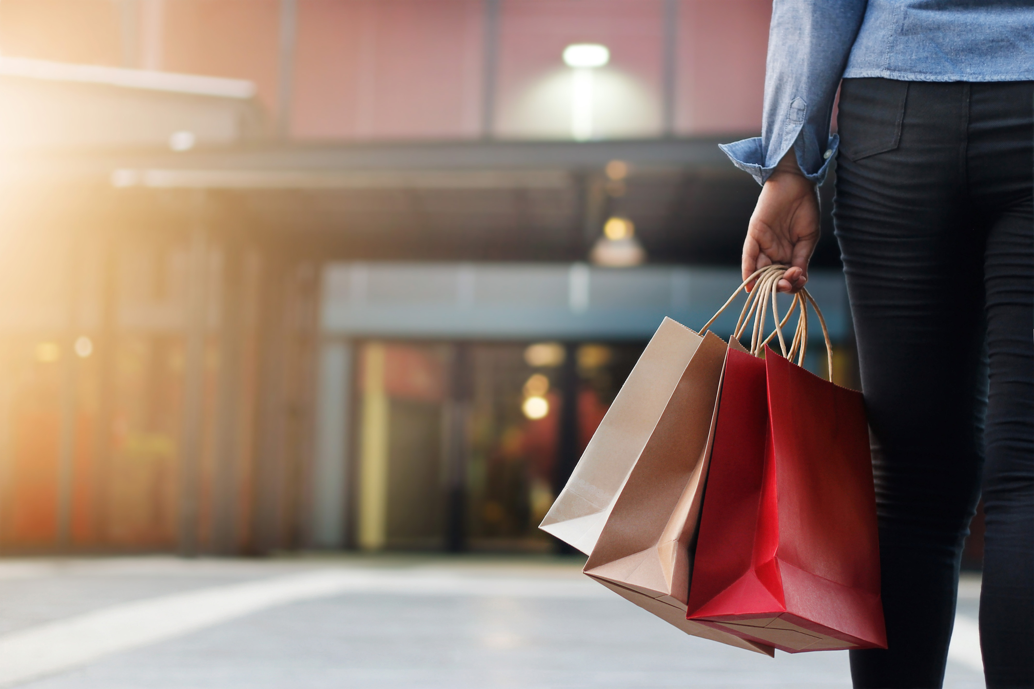 Shopper holding bags and heading towards mall entrance.