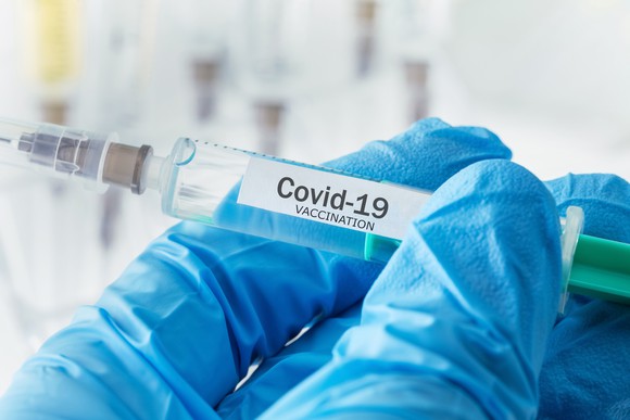 Gloved hands holding COVID-19 vaccine syringe