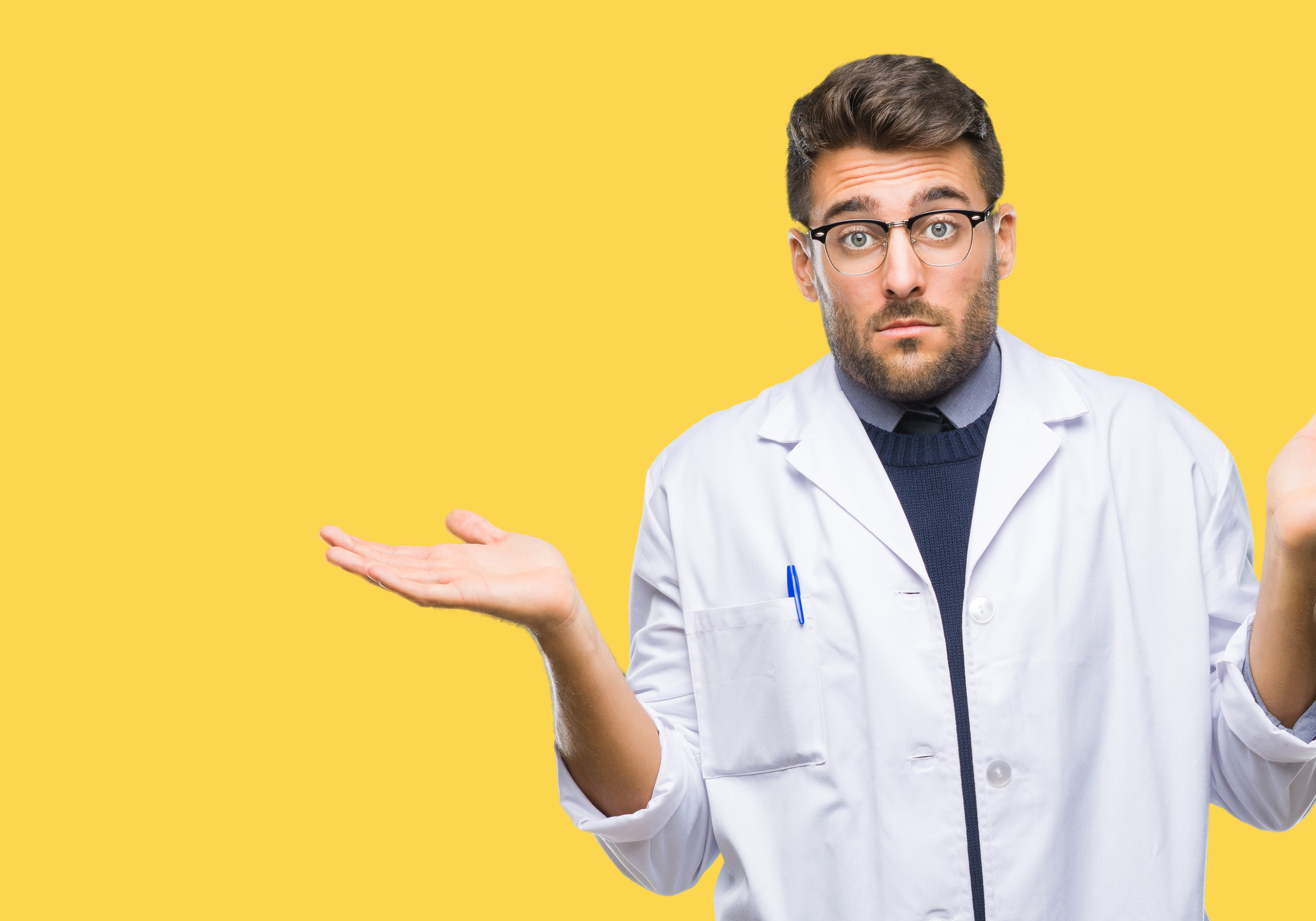 Young male doctor wearing a lab coat with his hands in the air and a confused look on his face.