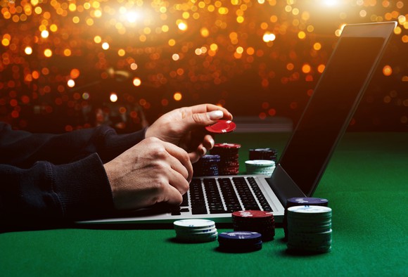 Person on a laptop holding casino chips.