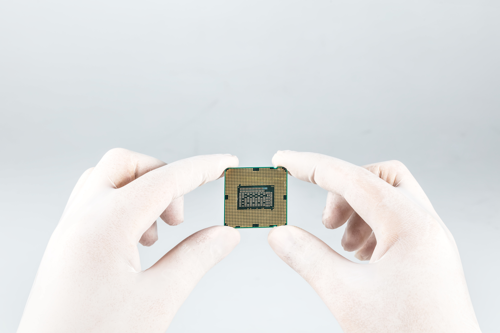 CPU held by the fingertips of someone wearing white rubber gloves.