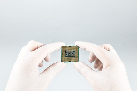 CPU held by the fingertips of someone wearing white rubber gloves.