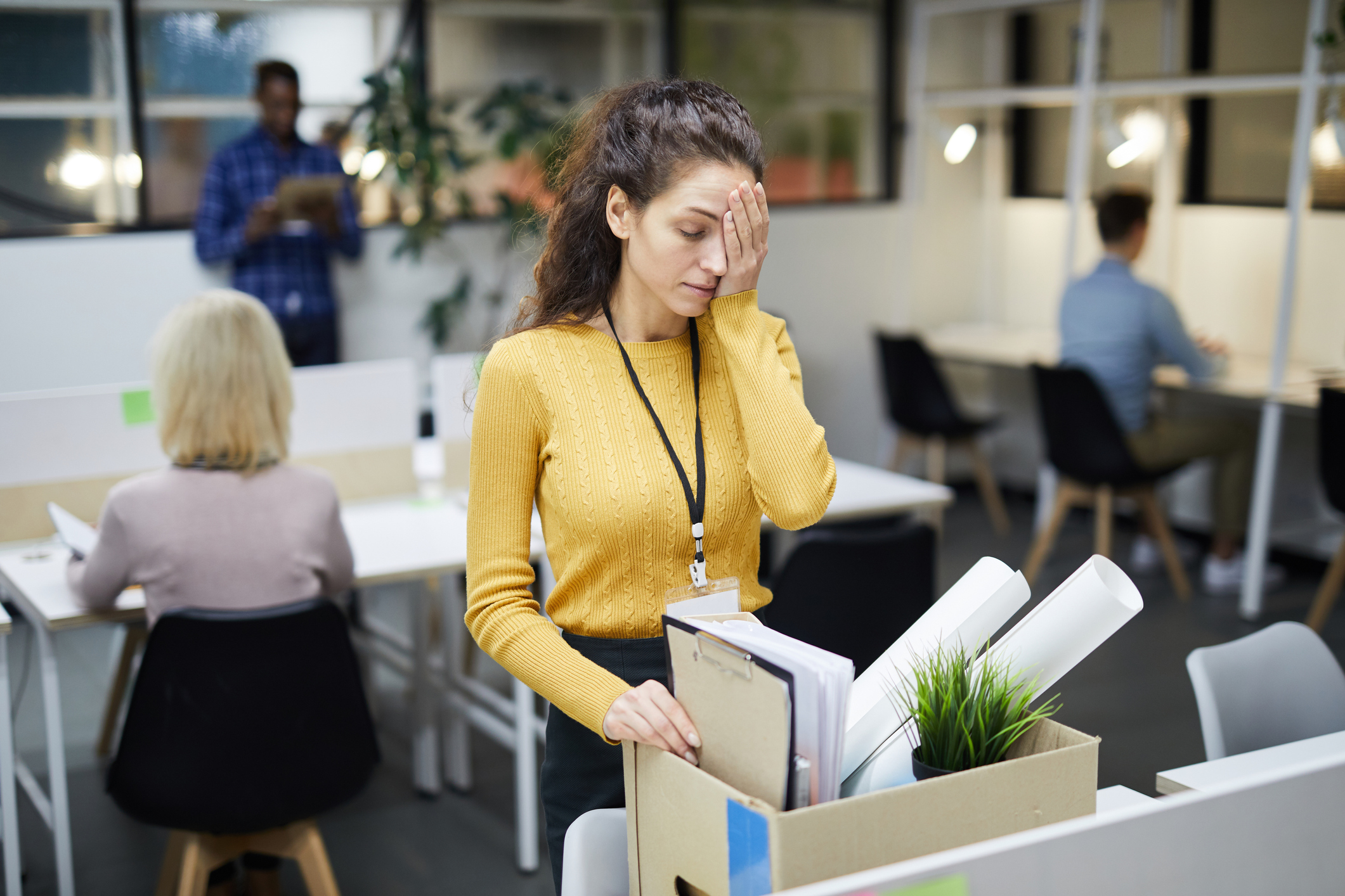 A woman with her hand over her forehead cleaning out her office desk