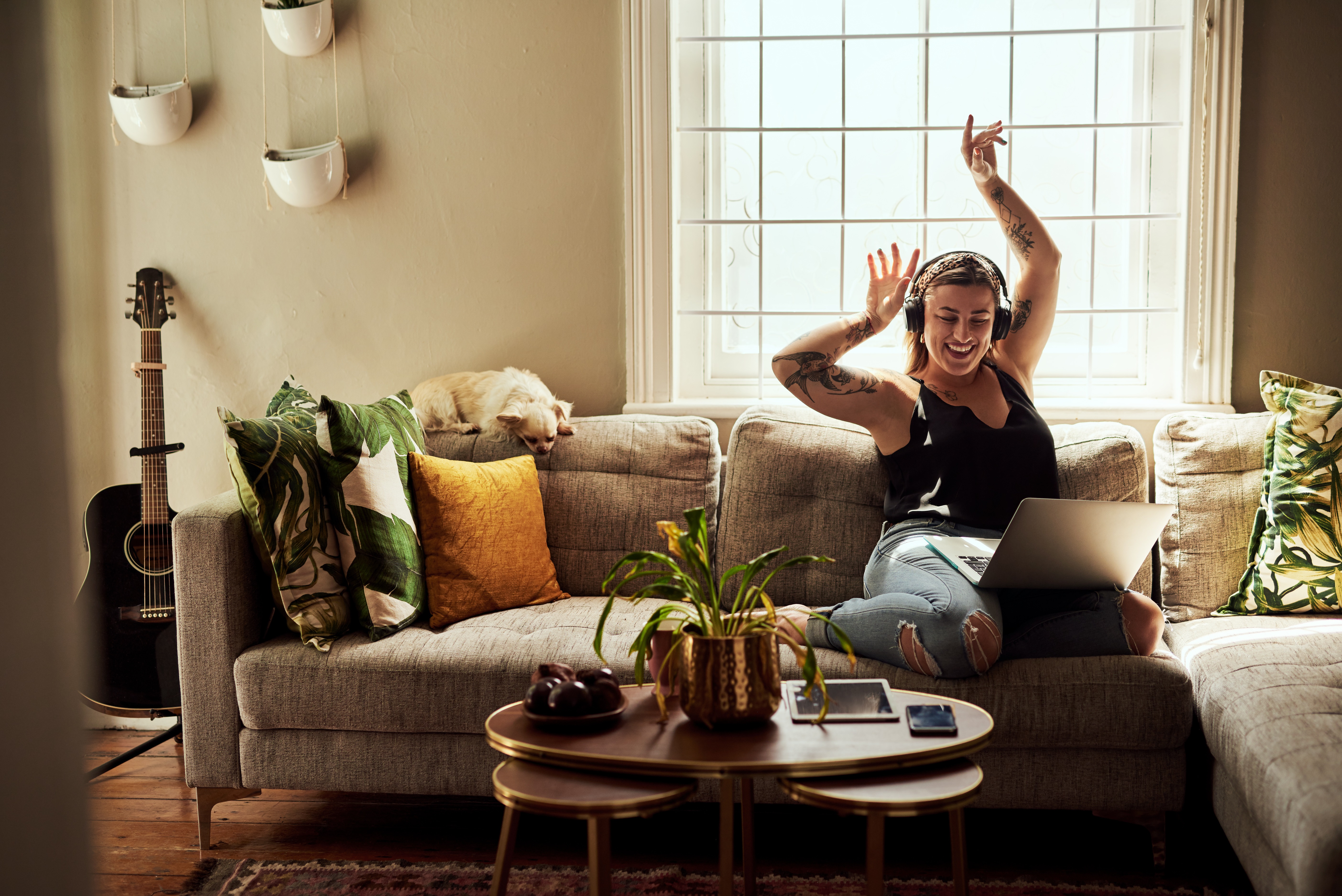 A woman wearing headphones and waving her arms in the air while sitting on a couch.
