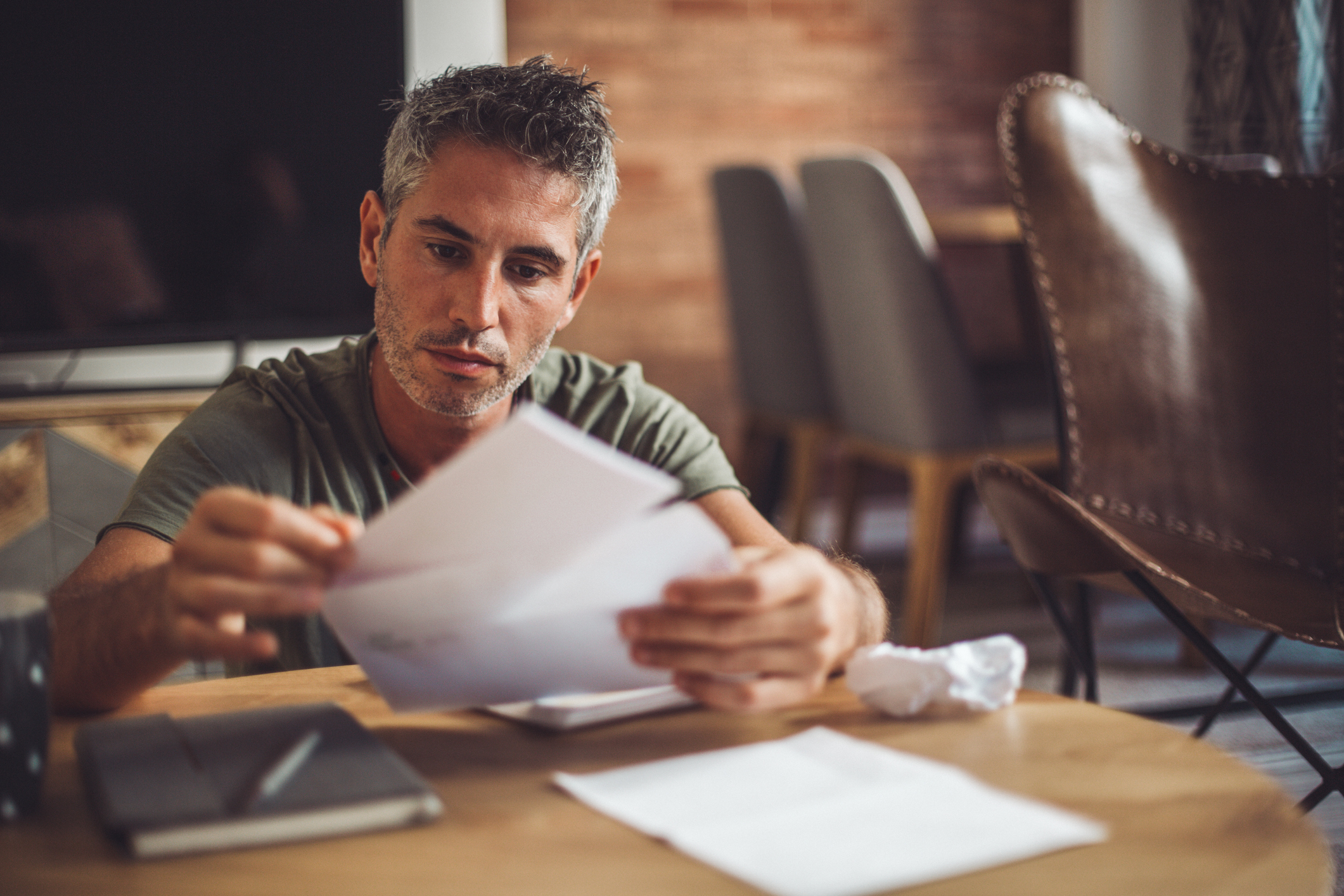 Man at table with serious expression holding envelope and folded piece of paper