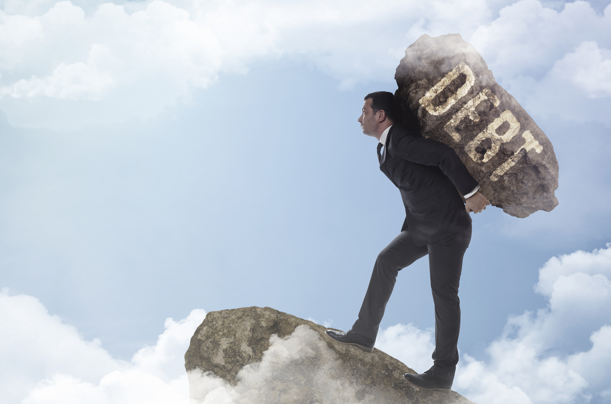 Man in a suit carrying a large rock labeled debt on his back up a mountain