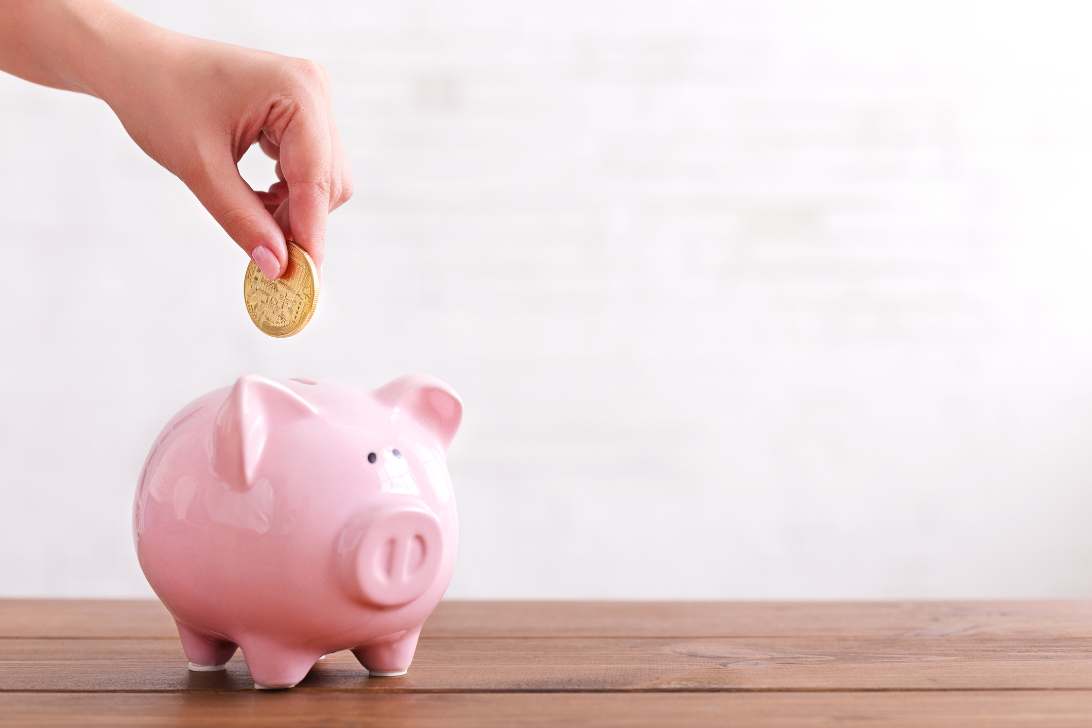 Hand putting coin in pink piggy bank.