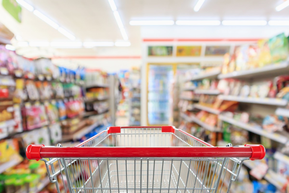 An empty grocery cart heading into a loaded supermarket aisle.