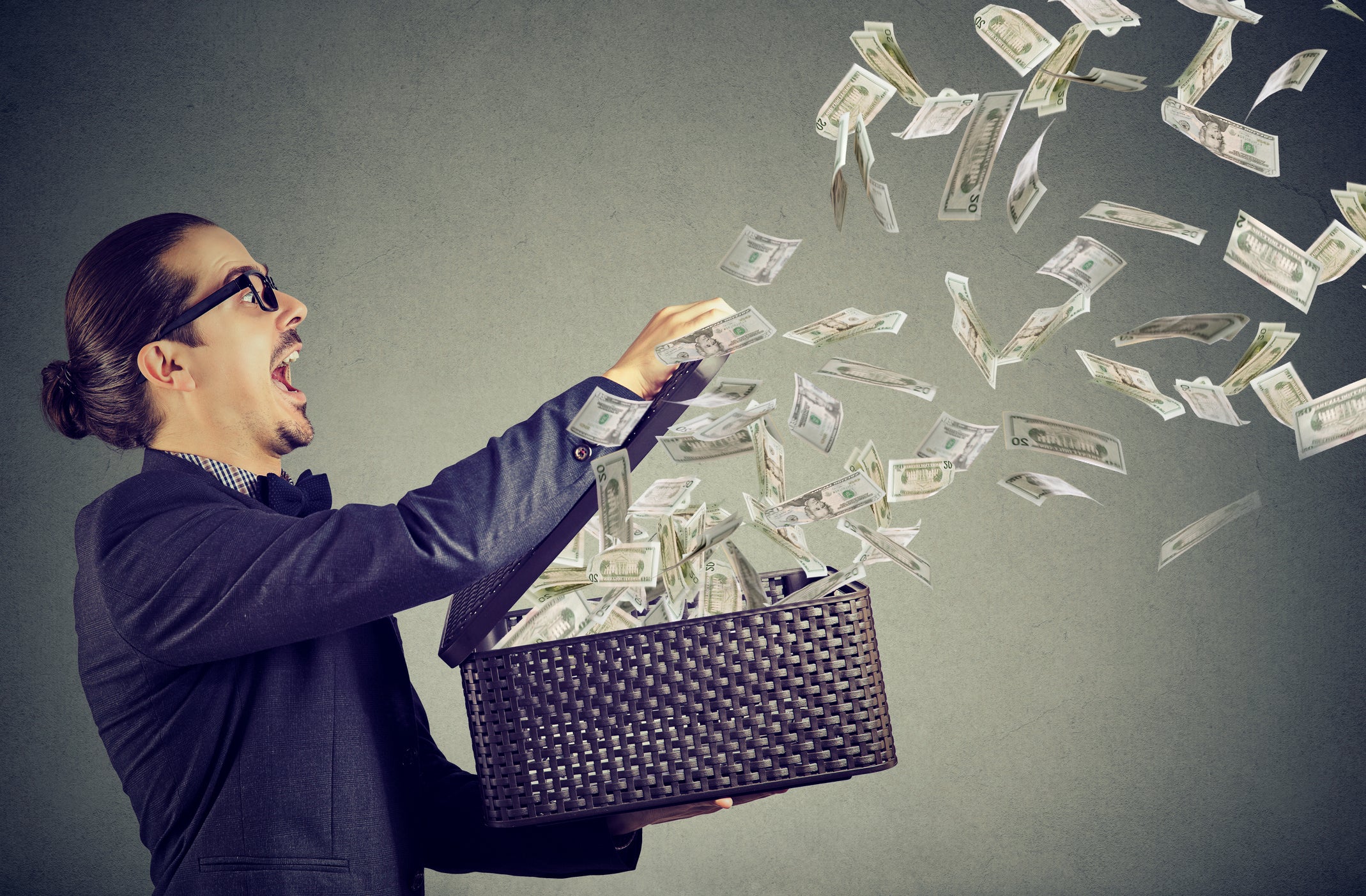 A man holding a suitcase open as money flies out.