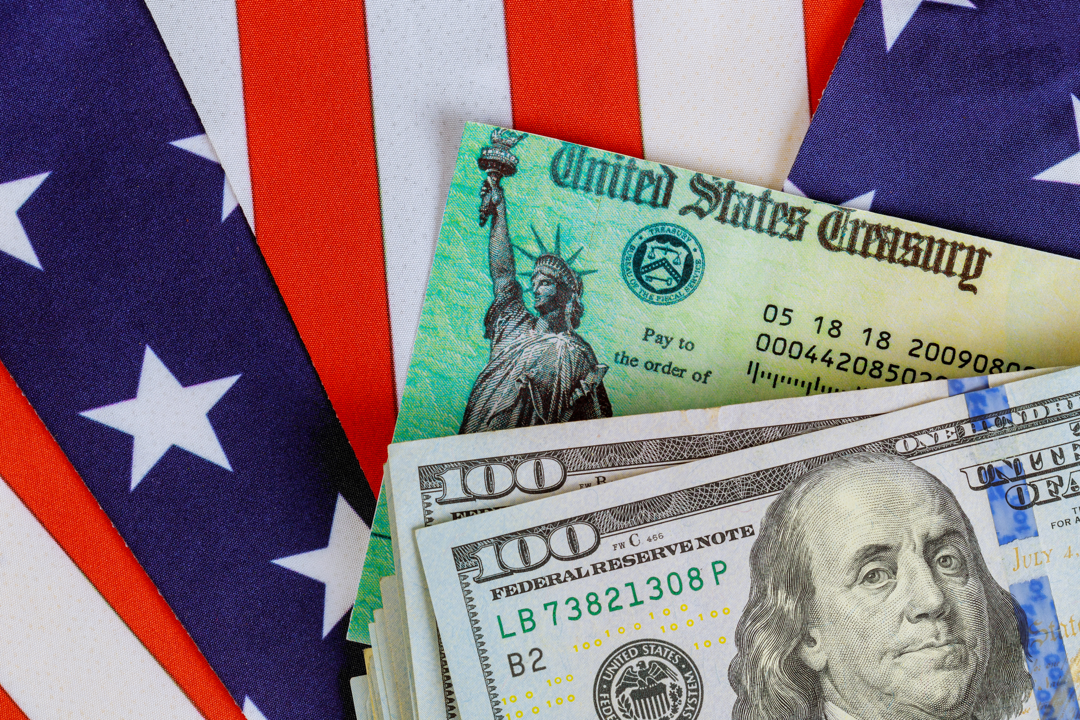 A pile of one hundred dollar bills and a U.S. Treasury check surrounded by an American flag.