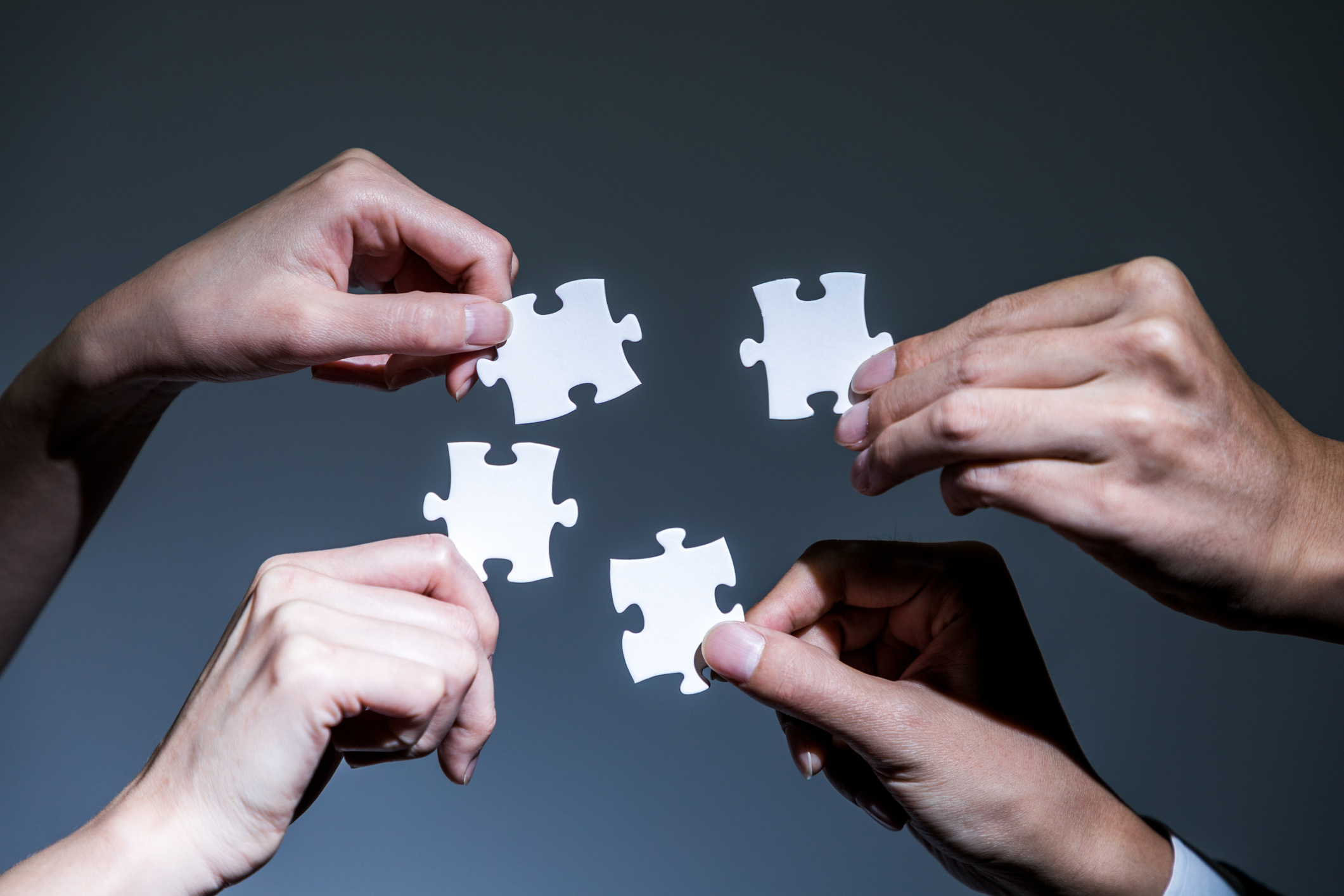 Fours hands holding pieces of jigsaw puzzle