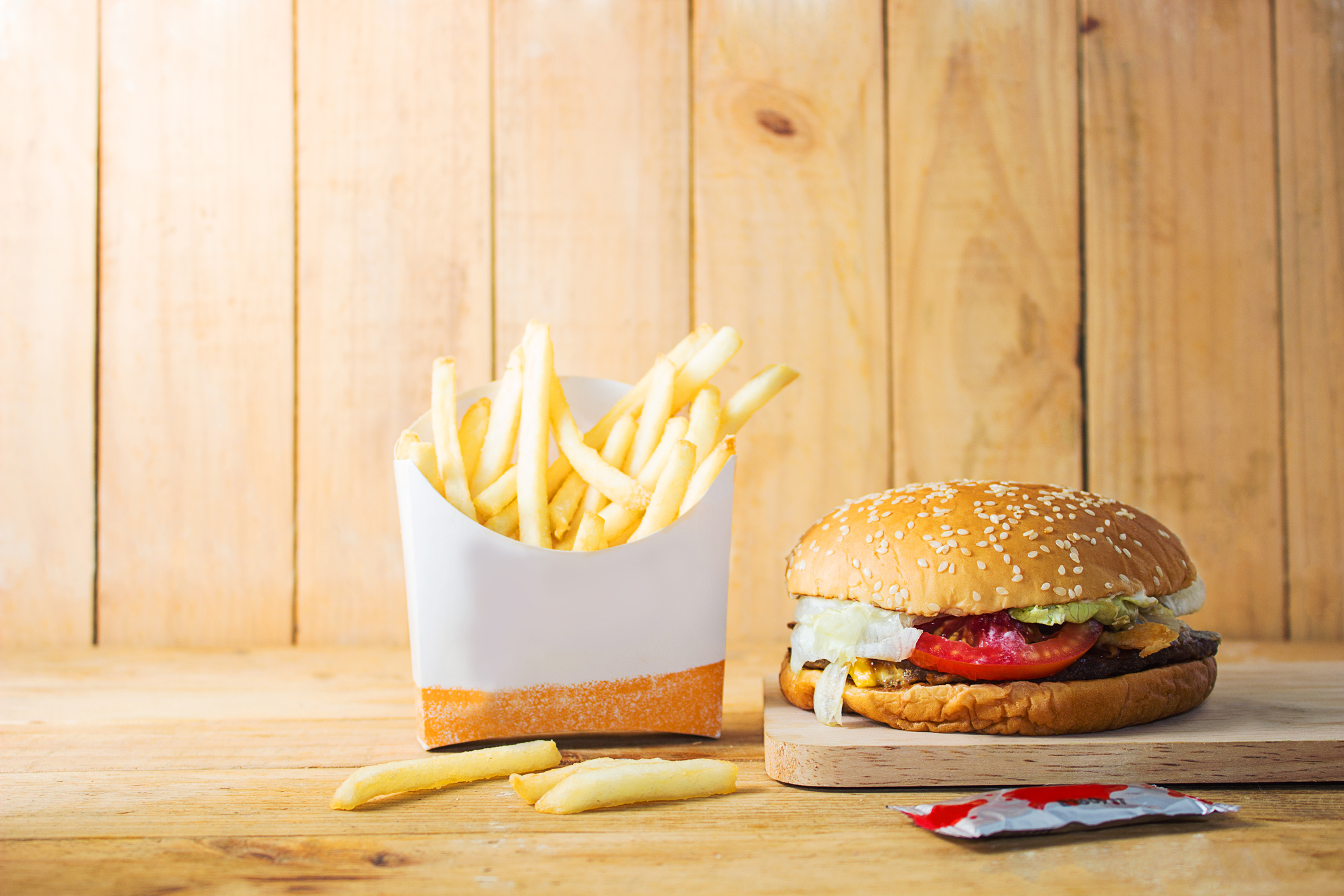 A hamburger and french fries sit on a table against a wood panel background.