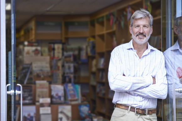Smiling man with arms crossed standing in doorway of bookstore